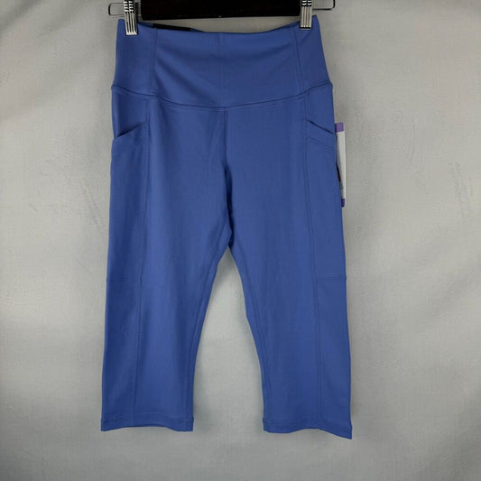Blue high-waisted cropped leggings with side pockets, hanging on a black hanger against a light gray textured background.