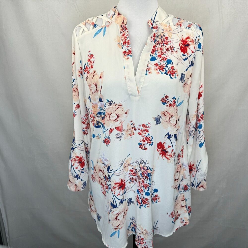 A women's long-sleeve blouse with a white base and a vibrant floral print in red, pink, and blue, displayed on a mannequin torso against a neutral gray backdrop.