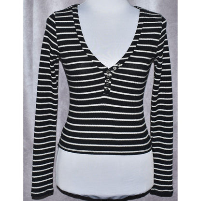 A black and white horizontally striped long-sleeve henley top displayed on a white mannequin torso against a gray curtain background.