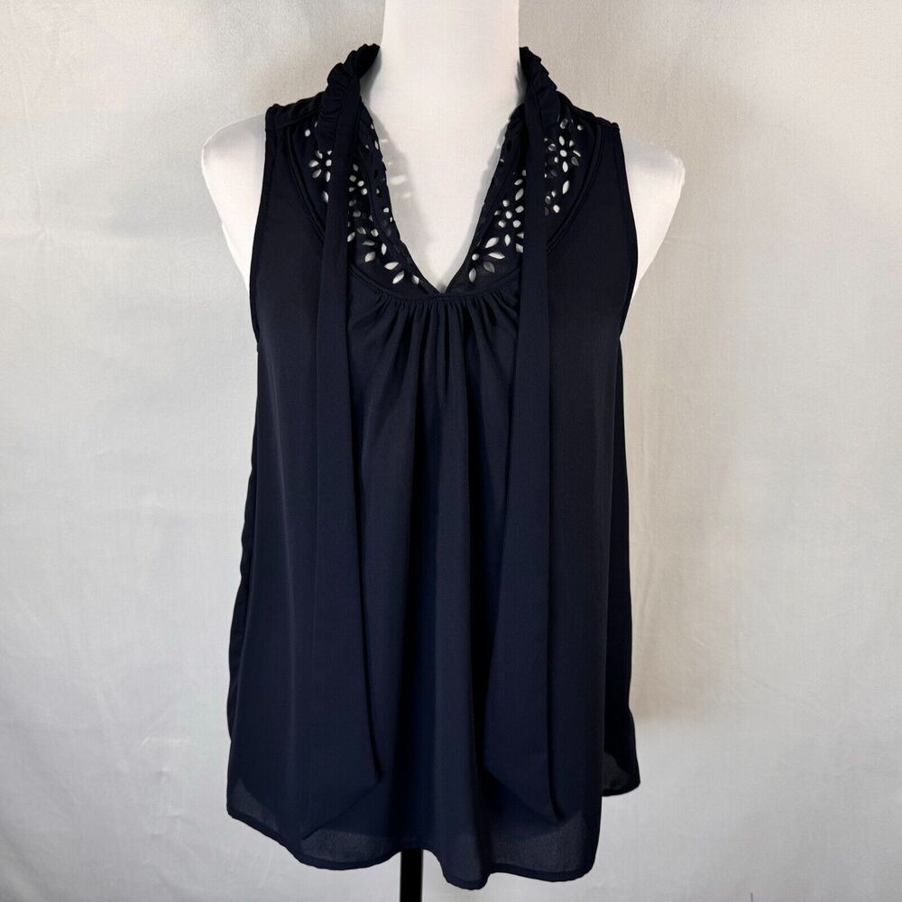 A sleeveless navy blue blouse with a gathered V-neckline and decorative cutout lace detailing around the collar, displayed on a white mannequin torso against a light gray fabric backdrop.