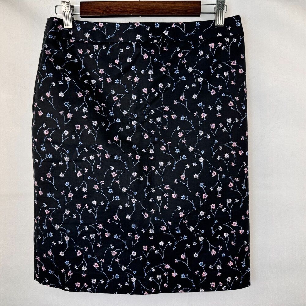 A black skirt with a delicate pink and blue floral vine pattern, hanging on a wooden hanger against a white background.