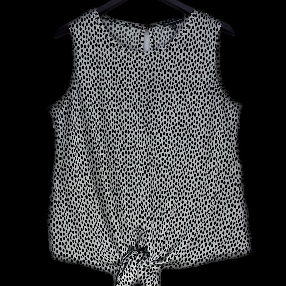 A sleeveless black and white spotted pattern top hanging on a black hanger against a solid black background.