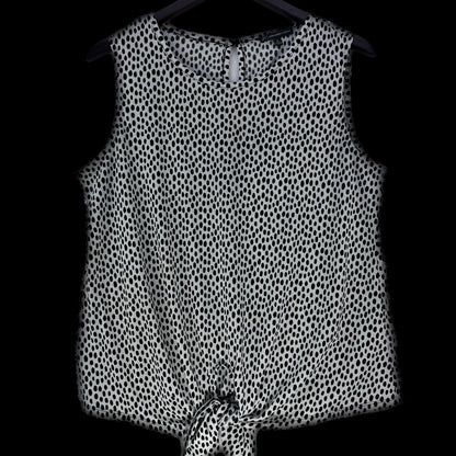 A sleeveless black and white spotted pattern top hanging on a black hanger against a solid black background.