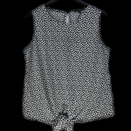 A sleeveless black and white spotted pattern top hanging on a black hanger against a solid black background.