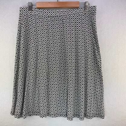 A black and white patterned pleated skirt hanging on a wooden hanger against a white wall.