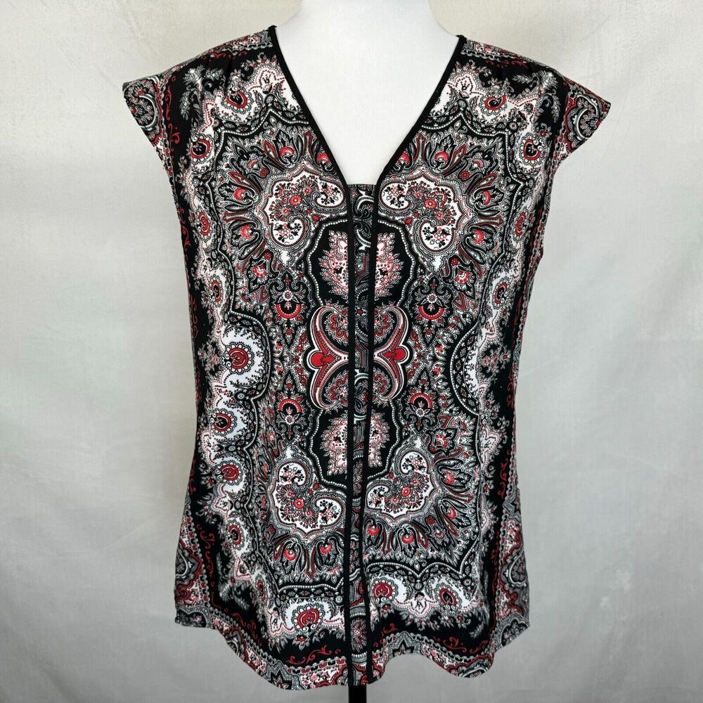 A sleeveless V-neck blouse with a black, white, and red paisley pattern, displayed on a white mannequin torso against a light gray fabric backdrop.