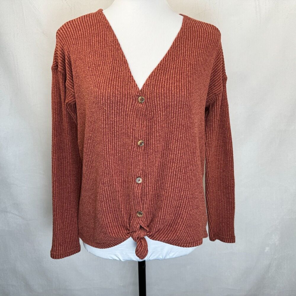 A rust-colored ribbed knit cardigan sweater with a V-neck, button-front closure, and front knot detail, displayed on a white mannequin torso against a light gray fabric backdrop.