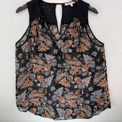 A sleeveless black lace-trim tank top with a paisley print in orange, gray, and white, hanging on a dark hanger against a light textured wall.