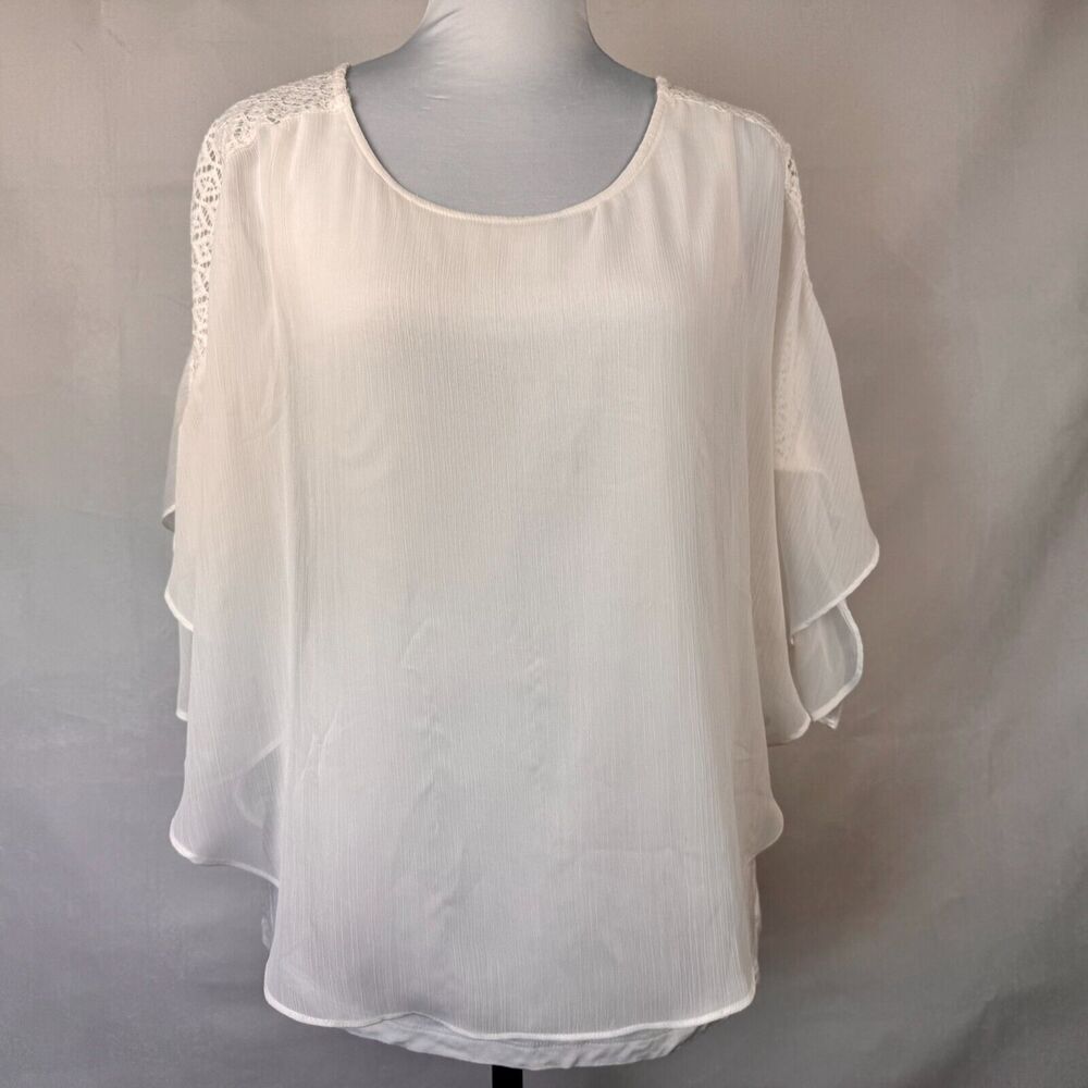 A white lightweight blouse with lace shoulder detailing, displayed on a gray mannequin torso against a neutral gray backdrop.