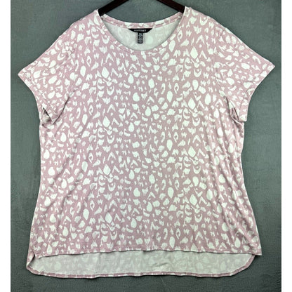 A short-sleeve scoop-neck top with an abstract white pattern on a dusty pink background, hanging on a dark hanger against a textured gray-green wall.