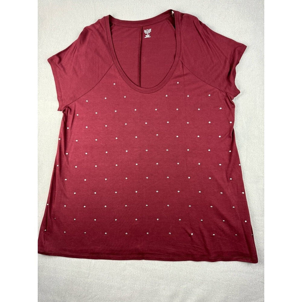 A women's short-sleeve scoop neck top in burgundy, decorated with a grid pattern of small white rhinestones, laid flat on a light beige fabric background.