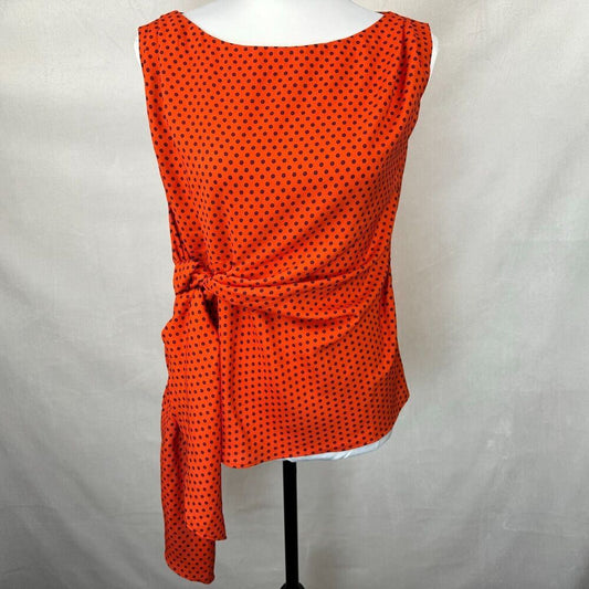 An orange sleeveless top with a black polka dot pattern, styled on a white mannequin torso with a side tie detail, set against a light gray fabric backdrop.