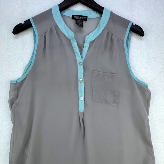 A sleeveless gray blouse with light blue trim on the collar, button placket, and pocket, hanging on a black hanger against a white textured background. The brand label reads 'amara & art'.