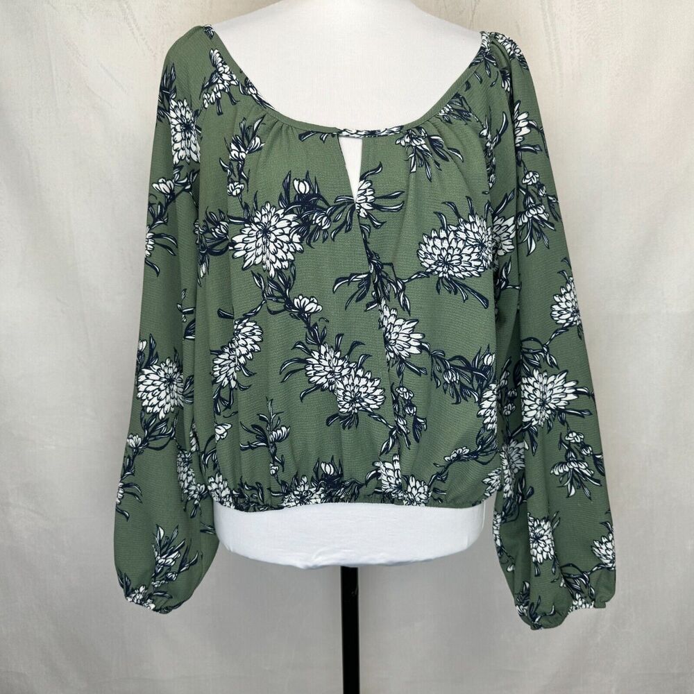 An olive green long-sleeve blouse with a white and navy floral print, displayed on a white mannequin torso against a neutral light gray fabric backdrop.