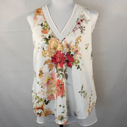 A sleeveless white V-neck blouse with a vibrant multicolor floral print, displayed on a white mannequin torso against a light gray fabric backdrop.