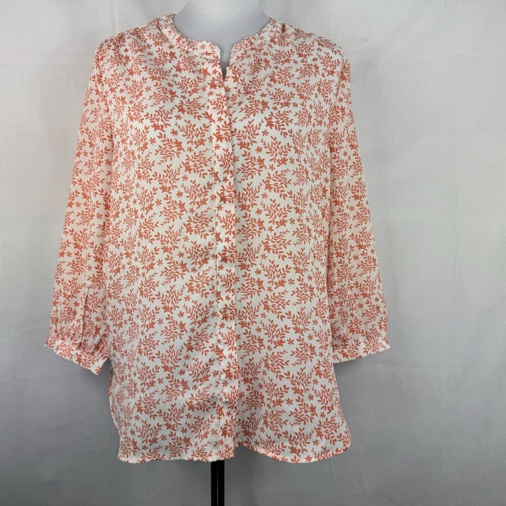 A long-sleeve blouse with a dense orange floral and leaf print on an off-white base, displayed on a mannequin torso against a light gray fabric backdrop.