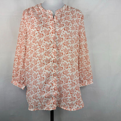 A long-sleeve blouse with a dense orange floral and leaf print on an off-white base, displayed on a mannequin torso against a light gray fabric backdrop.