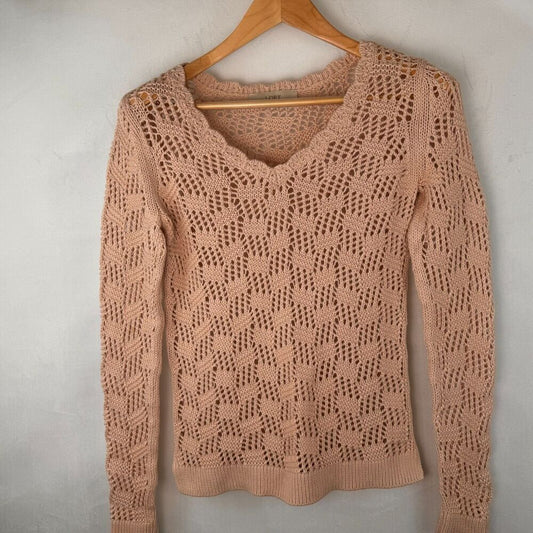 A peach-colored open-knit long-sleeve sweater hanging on a wooden hanger against a textured light gray wall.