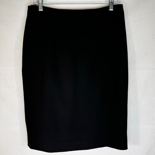 A black knee-length pencil skirt hanging from a metal hanger against a light gray textured wall.