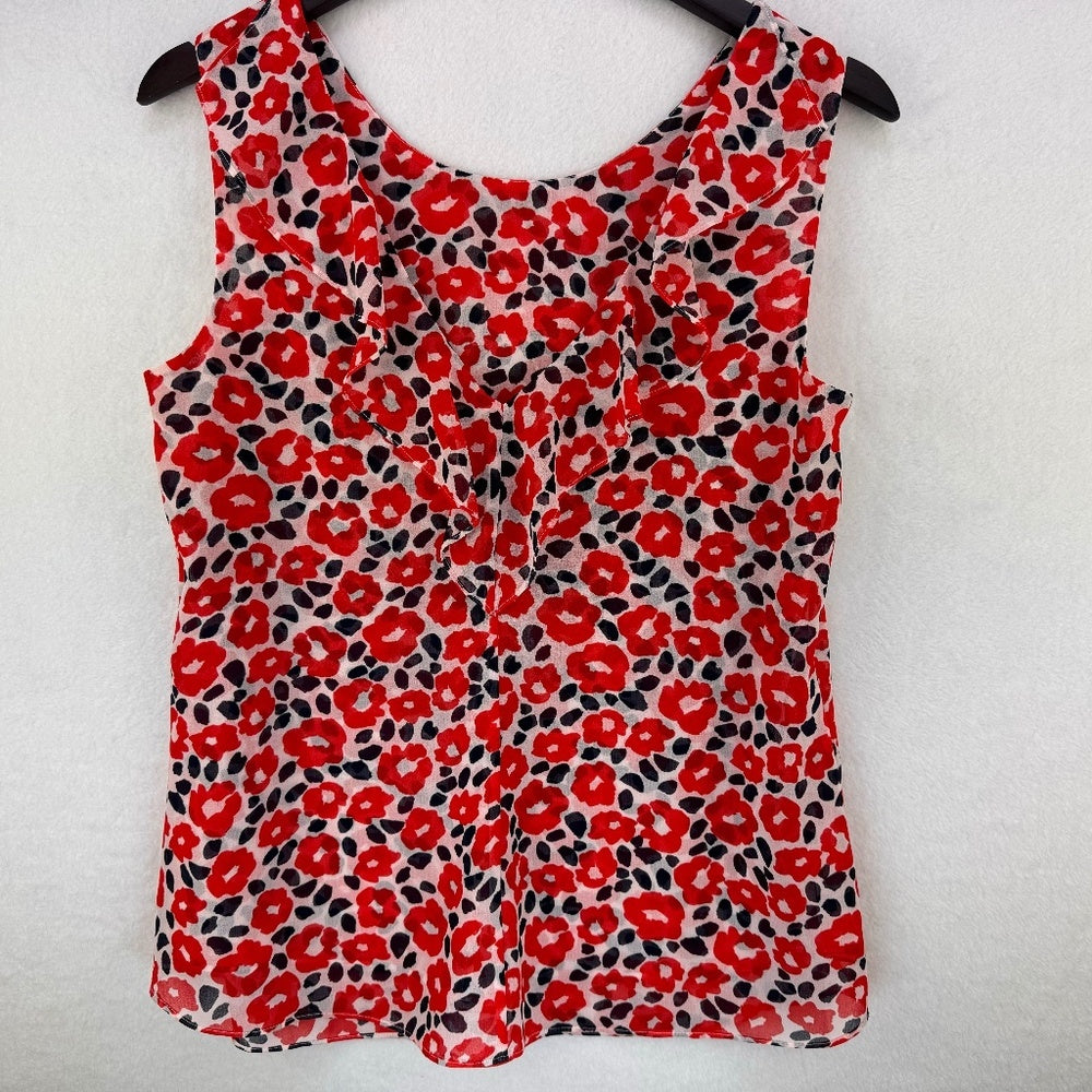 A sleeveless red floral print top hanging on a black hanger against a white textured wall.