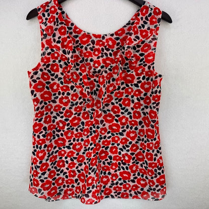 A sleeveless red floral print top hanging on a black hanger against a white textured wall.