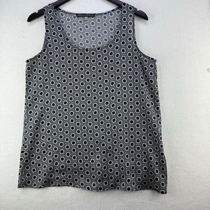 A sleeveless black tank top with a white geometric hexagon pattern, hanging on a black hanger against a light gray textured wall.