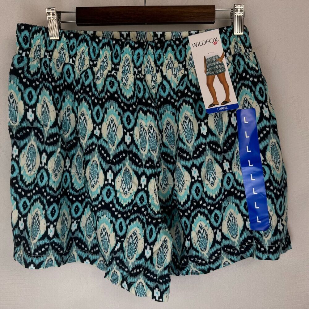 Wildfox brand patterned shorts in a teal, black, and white ikat design, hanging on a wooden hanger with retail tags attached.