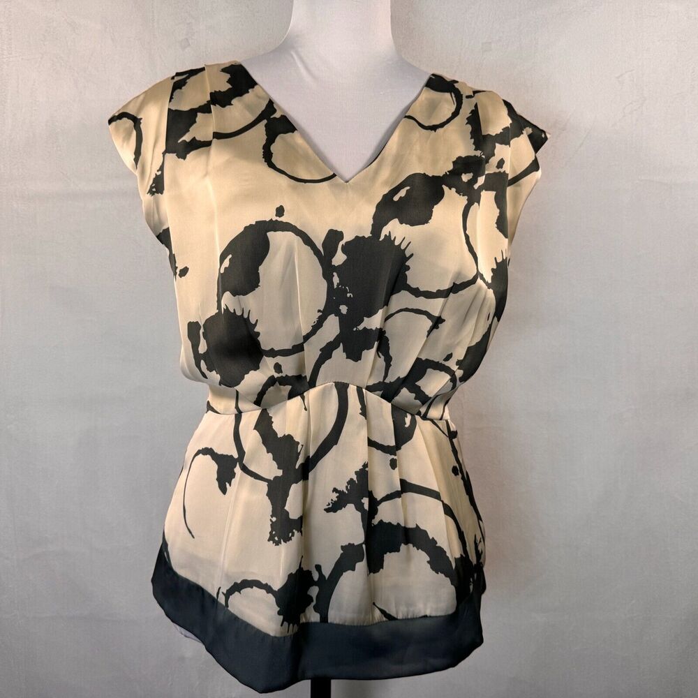 A beige satin-like top with a black abstract brushstroke pattern, displayed on a white mannequin torso against a light gray textured background.