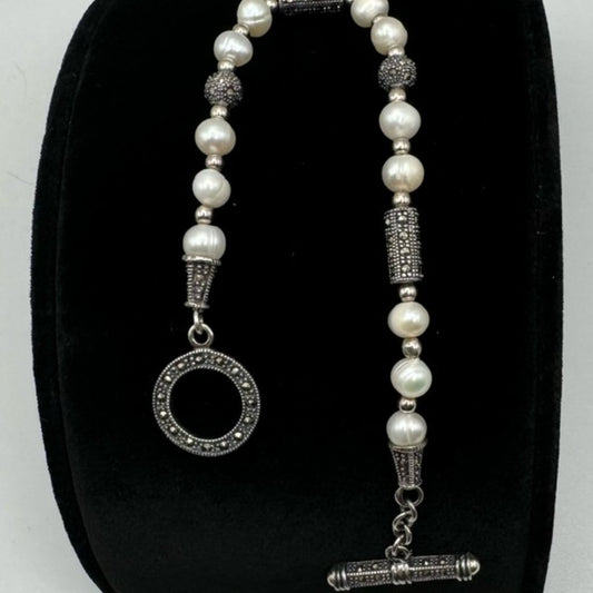 A beaded necklace with white pearls and silver-toned textured beads, displayed on a black velvet jewelry bust. The necklace features a circular pendant with a pavé border and a toggle clasp.
