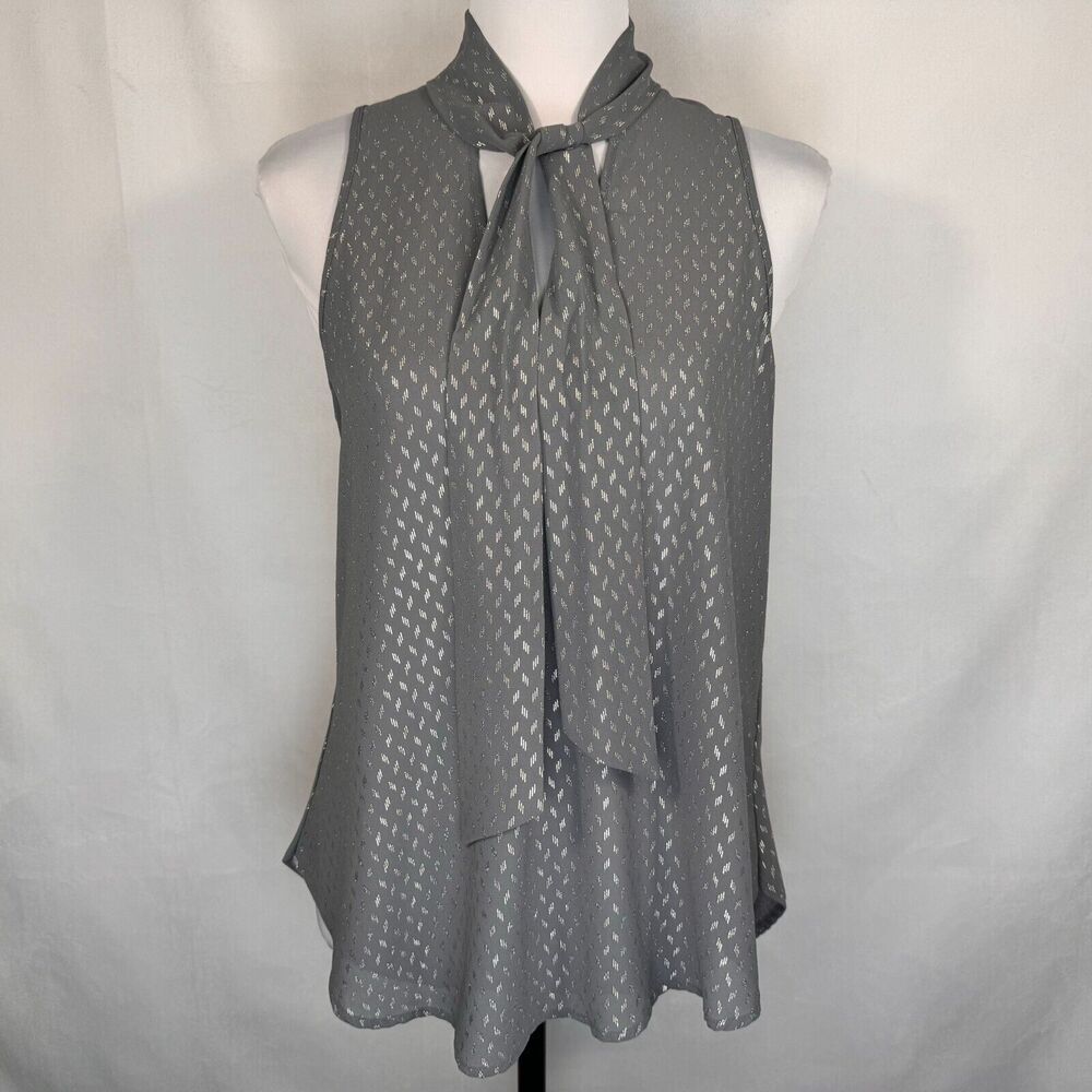 A gray sleeveless blouse with a tie-neck detail and a subtle repeating geometric pattern, displayed on a white mannequin torso against a light gray fabric backdrop.