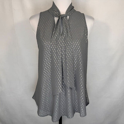 A gray sleeveless blouse with a tie-neck detail and a subtle repeating geometric pattern, displayed on a white mannequin torso against a light gray fabric backdrop.